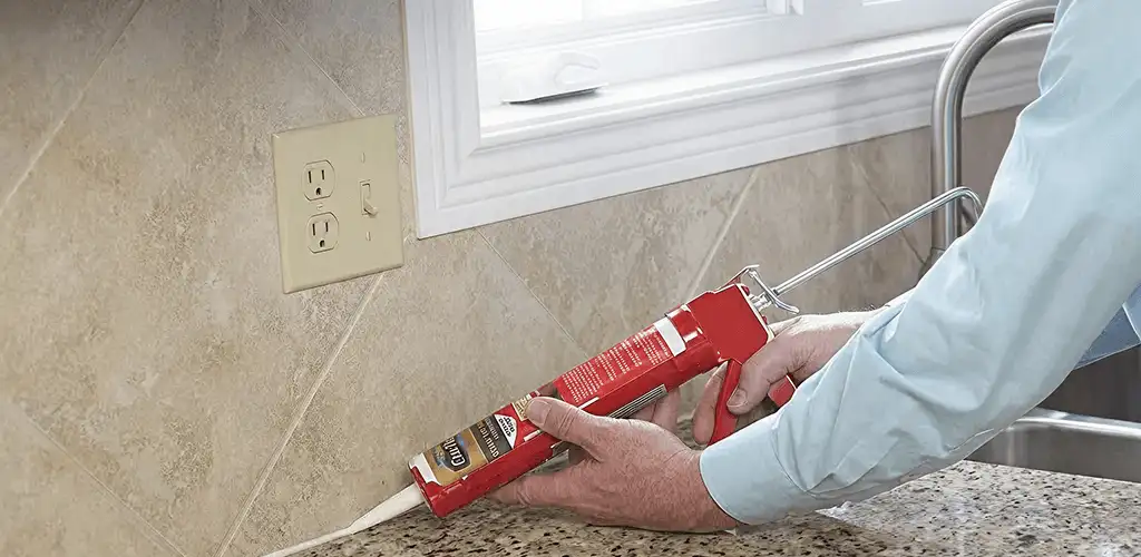 Handyman applying caulk along a kitchen backsplash and countertop seam in Indianapolis, IN